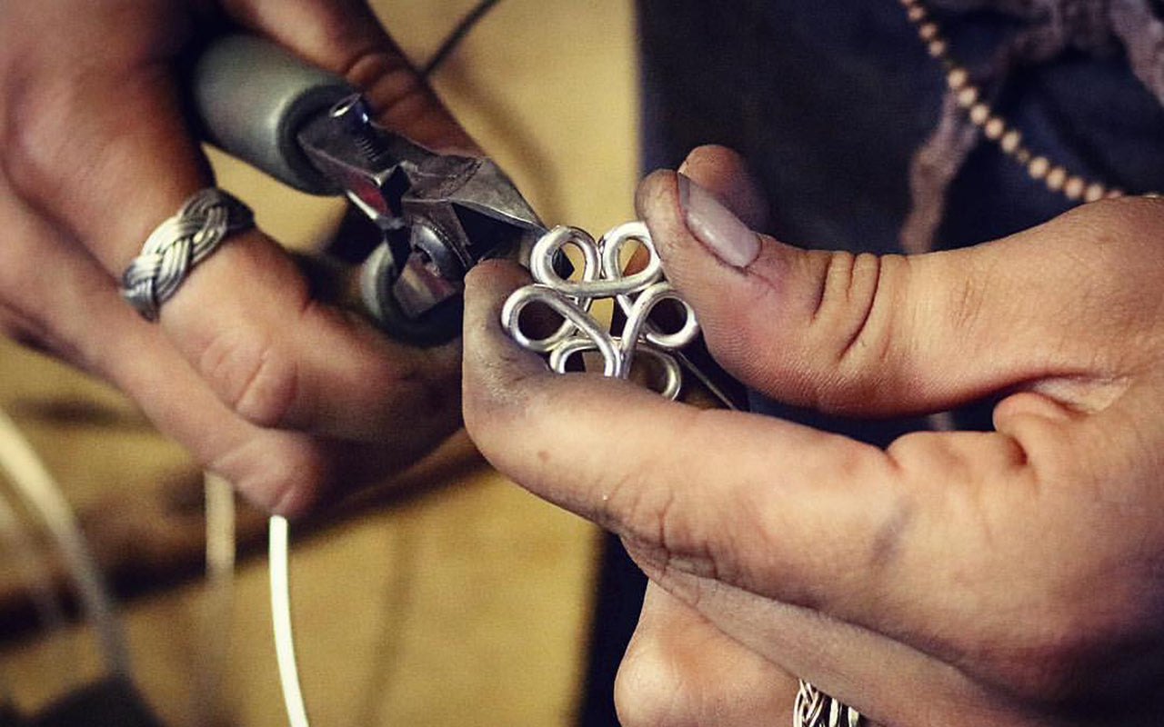 Close-up of hands working on a silver flower pendant with pliers.