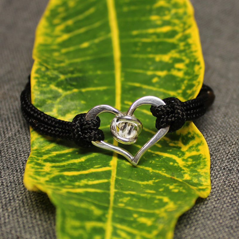 Black adjustable nylon cord bracelet with sterling silver heart and love knot piece in center.