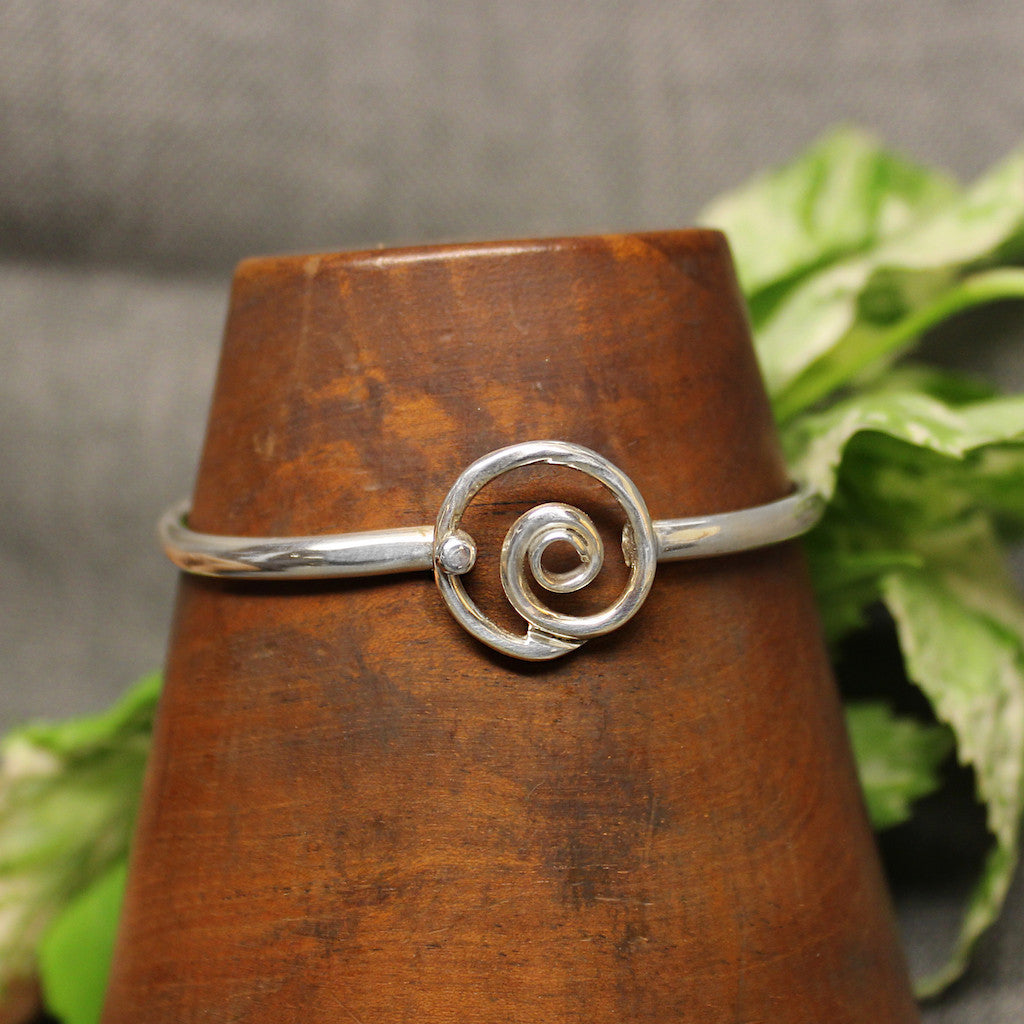 Thin sterling silver child's bracelet with spiral design in center.
