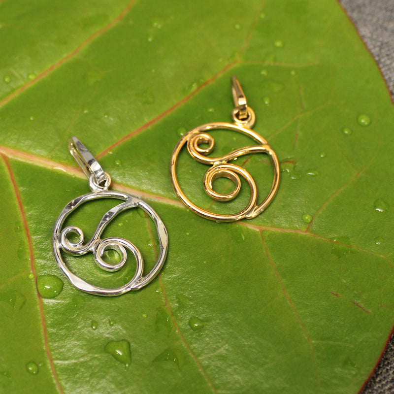 Circular 14k gold and sterling silver pendants with delicate rolling wave design in center.