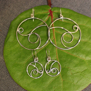 Small and large sterling silver hoop earrings with delicate rolling wave design in center.