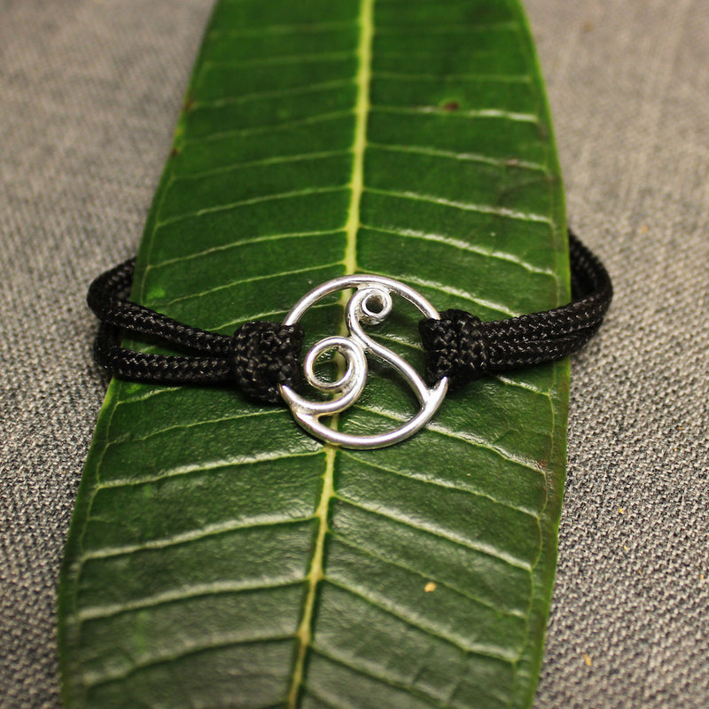 Adjustable black nylon cord bracelet with sterling silver circular design in center containing a delicate rolling wave.